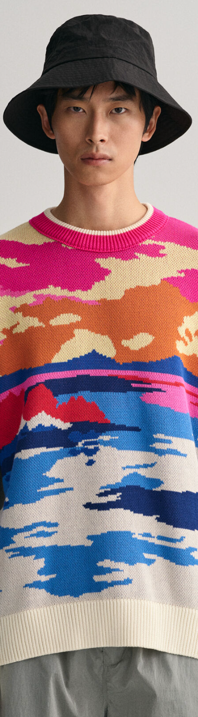A man wearing a Gant sunset sweater, grey pants and a black bucket hat