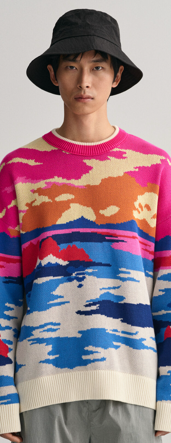 A man wearing a Gant sunset sweater, grey pants and a black bucket hat