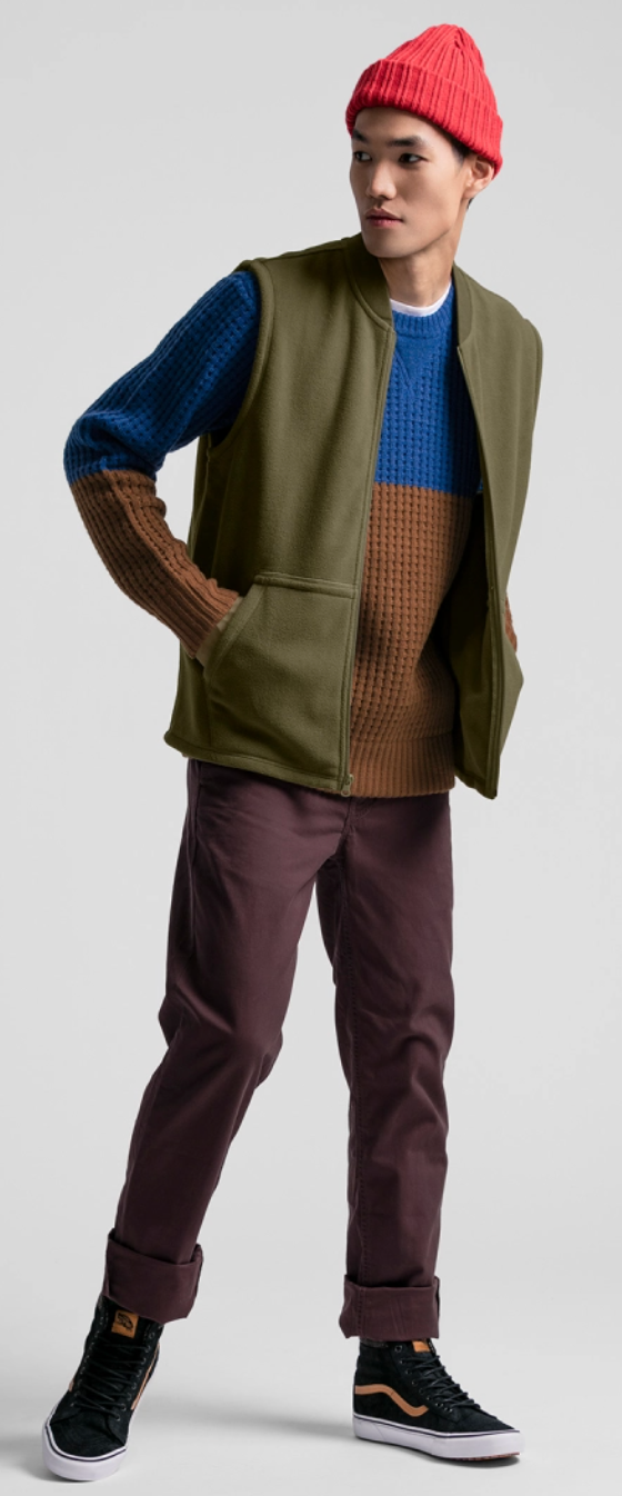 A man wearing a JackThreads outfit featuring a red beanie. green vest and red pants