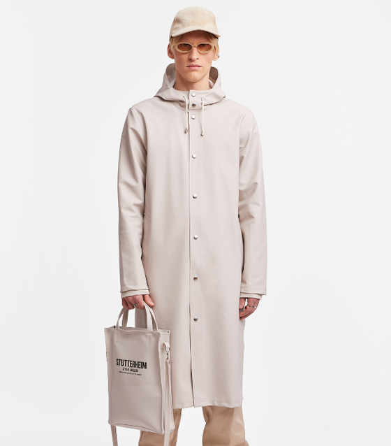 A man wearing a contemporary beige Stutterheim raincoat with matching hat and sunglasses