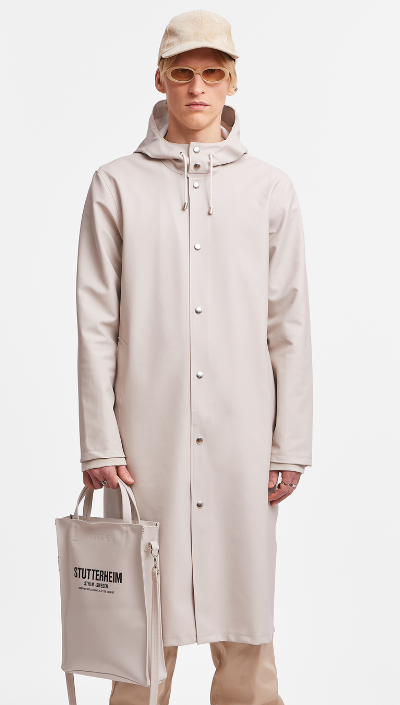 A man wearing a contemporary beige Stutterheim raincoat with matching hat and sunglasses