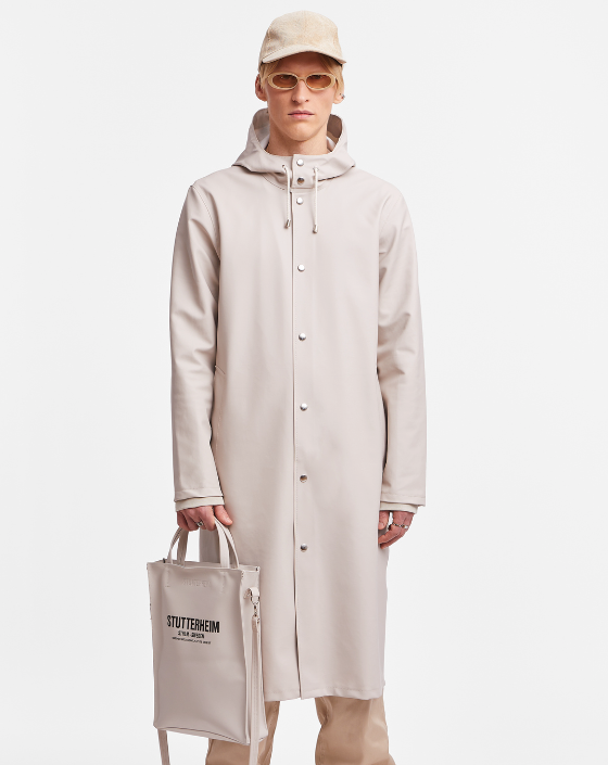 A man wearing a contemporary beige Stutterheim raincoat with matching hat and sunglasses