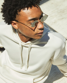 A man sitting looking away wearing a Alternative Apparel cream hoodie with sunglasses