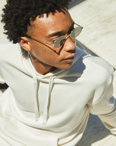 A man sitting looking away wearing a Alternative Apparel cream hoodie with sunglasses