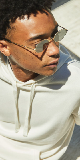 A man sitting looking away wearing a Alternative Apparel cream hoodie with sunglasses