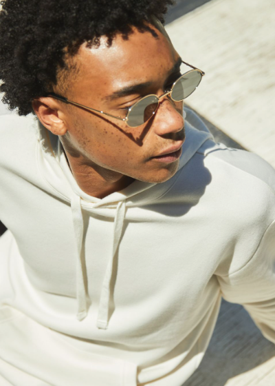 A man sitting looking away wearing a Alternative Apparel cream hoodie with sunglasses