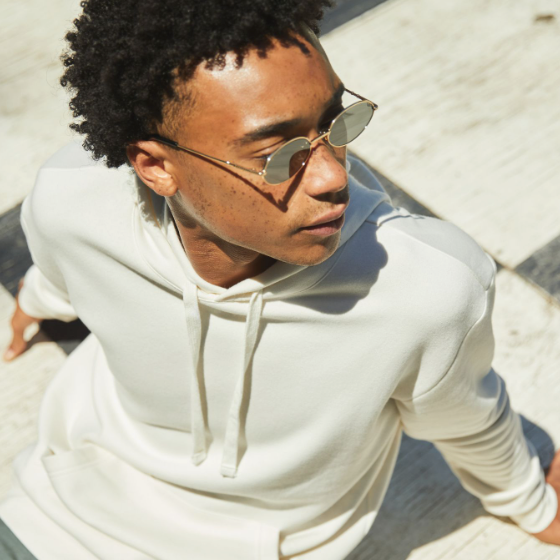 A man sitting looking away wearing a Alternative Apparel cream hoodie with sunglasses