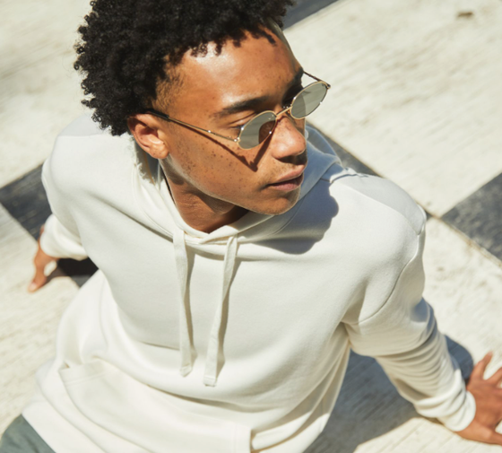 A man sitting looking away wearing a Alternative Apparel cream hoodie with sunglasses