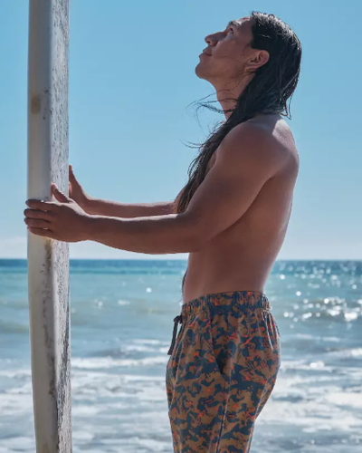 A man standing with a surf-board with colorful print swim shorts by PrAna