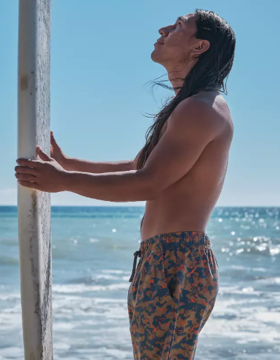 A man standing with a surf-board with colorful print swim shorts by PrAna