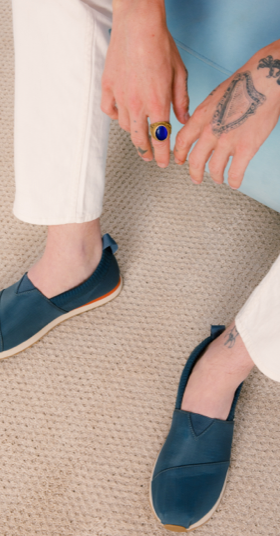 A man sitting wearing navy blue slip-on Tom's shoes