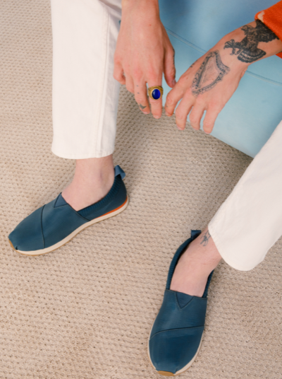 A man sitting wearing navy blue slip-on Tom's shoes