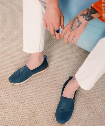 A man sitting wearing navy blue slip-on Tom's shoes