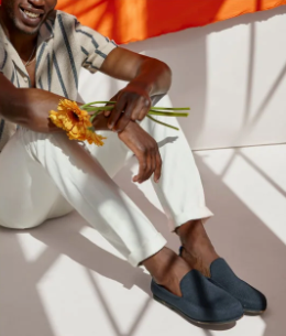 A man sitting with flowers in his hand and Rothy's slip-on shoes on his feet