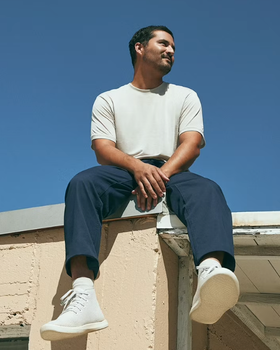 A man sitting on a roof in an Allbirds outfit featuring grey shoes
