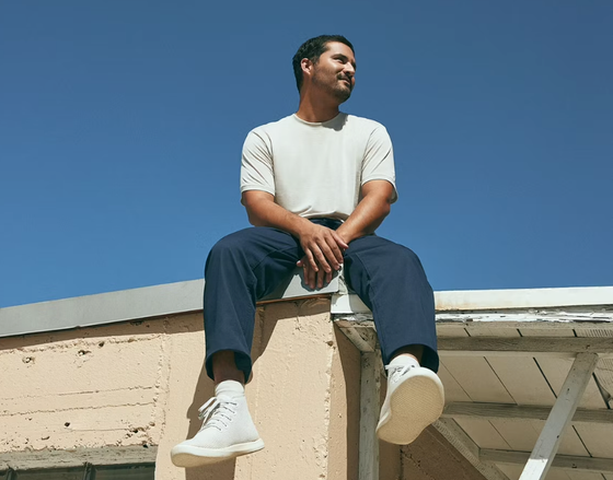 A man sitting on a roof in an Allbirds outfit featuring grey shoes