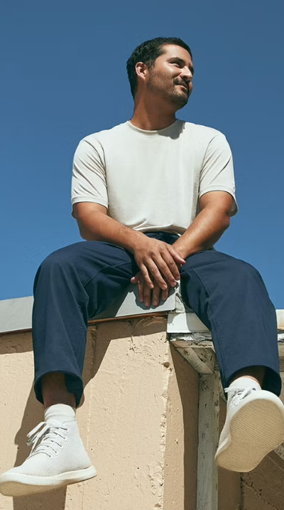 A man sitting on a roof in an Allbirds outfit featuring grey shoes