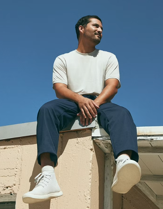 A man sitting on a roof in an Allbirds outfit featuring grey shoes