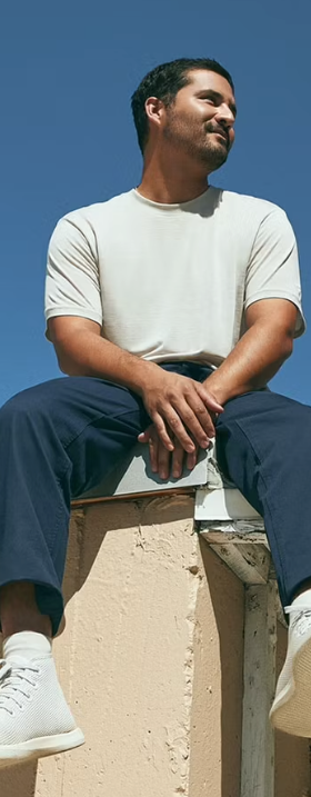 A man sitting on a roof in an Allbirds outfit featuring grey shoes