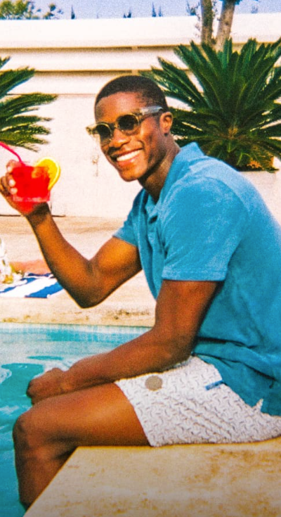 A man sitting by a pool in Ted Baker swimshorts and a blue polo