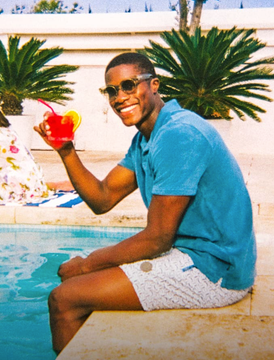 A man sitting by a pool in Ted Baker swimshorts and a blue polo