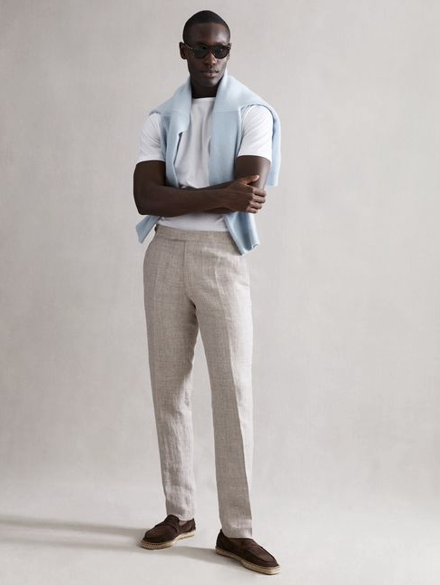 A man wearing a modern country club outfit by Reiss with a baby blue sweater draped across his shoulders