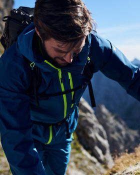 A man hiking in a blue and green Jack Wolfskin jacket and pants