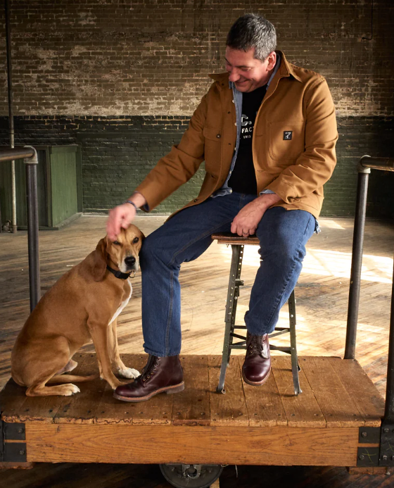 A man sitting with a dog wearing a LC King outfit featuring modern workwear