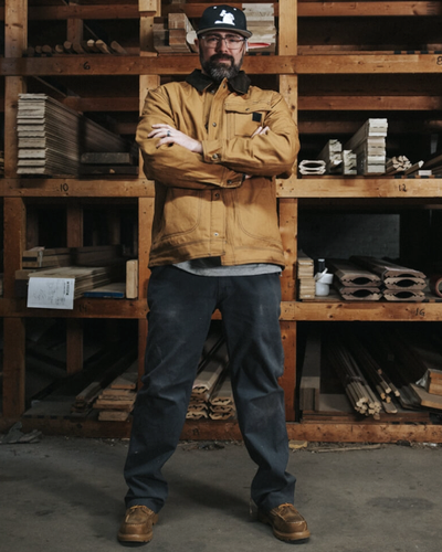 A man wearing a Wolverine brown jacket with his arms crossed