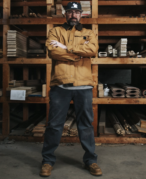 A man wearing a Wolverine brown jacket with his arms crossed