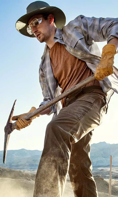 A man working with a pickaxe wearing Duluth Trading Co. workwear