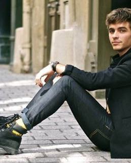 A man sitting wearing black Caterpillar work boots with the yellow logo branded across it