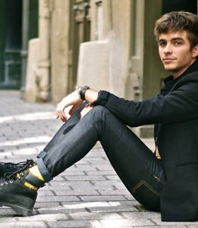 A man sitting wearing black Caterpillar work boots with the yellow logo branded across it