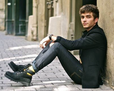 A man sitting wearing black Caterpillar work boots with the yellow logo branded across it