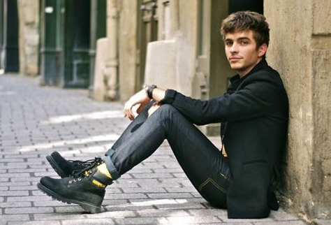 A man sitting wearing black Caterpillar work boots with the yellow logo branded across it