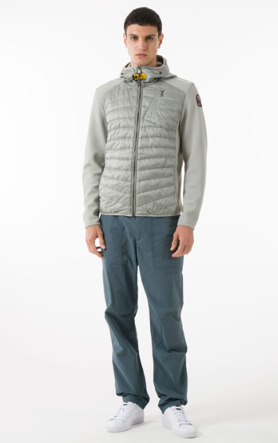 A man wearing a light grey Parajumpers puffy jacket along with blue pants and white shoes