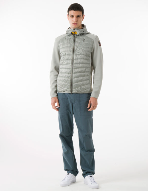 A man wearing a light grey Parajumpers puffy jacket along with blue pants and white shoes