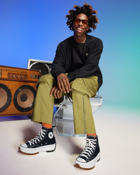 A man sitting beside a speaker wearing platform Converse in black and white