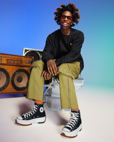 A man sitting beside a speaker wearing platform Converse in black and white