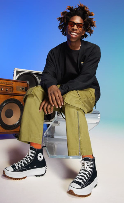 A man sitting beside a speaker wearing platform Converse in black and white
