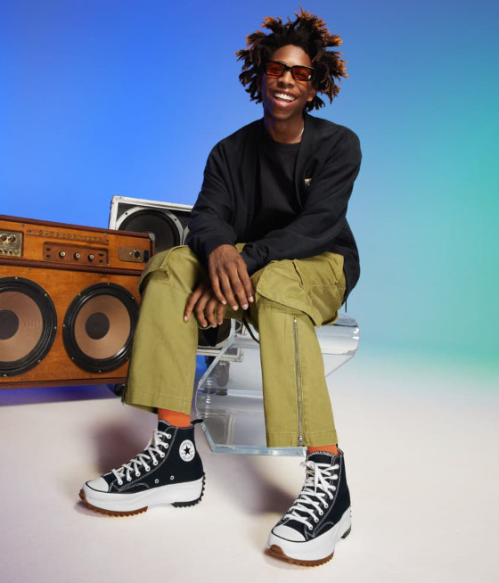 A man sitting beside a speaker wearing platform Converse in black and white