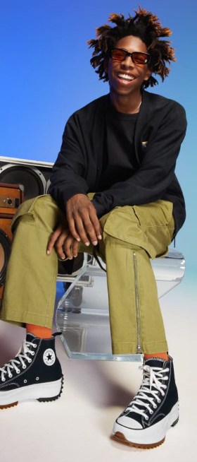 A man sitting beside a speaker wearing platform Converse in black and white