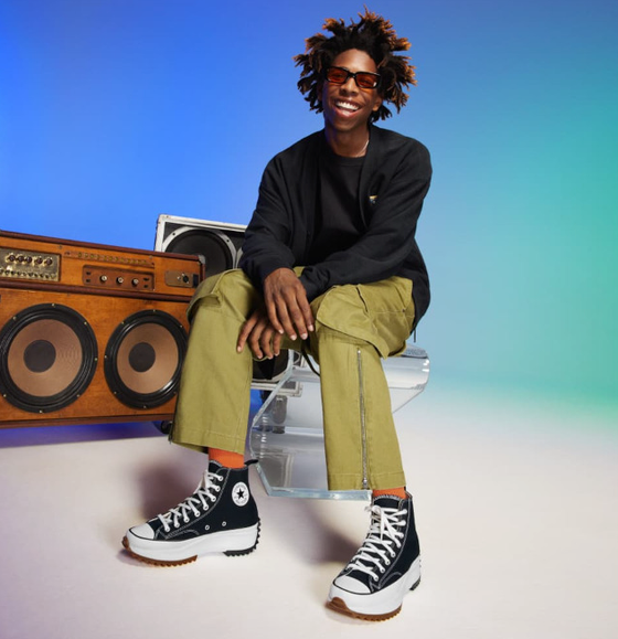 A man sitting beside a speaker wearing platform Converse in black and white