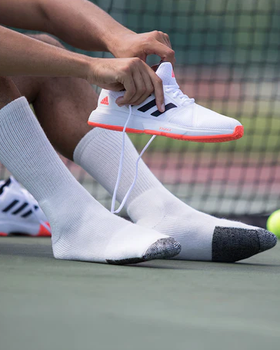 A man putting on tennis shoes wearing white Thorlo Socks