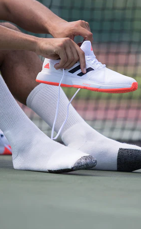 A man putting on tennis shoes wearing white Thorlo Socks