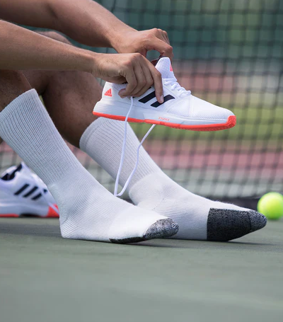 A man putting on tennis shoes wearing white Thorlo Socks