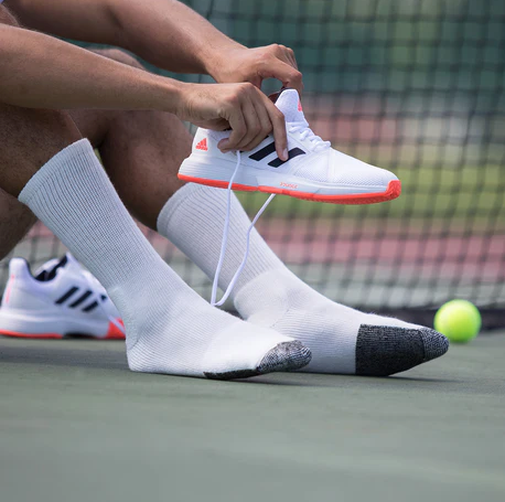 A man putting on tennis shoes wearing white Thorlo Socks