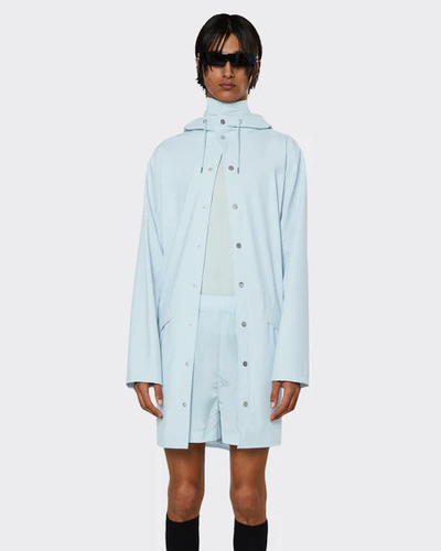A man wearing a baby blue Rains raincoat with matching shorts and black sunglasses