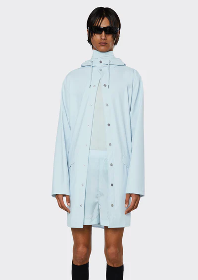 A man wearing a baby blue Rains raincoat with matching shorts and black sunglasses