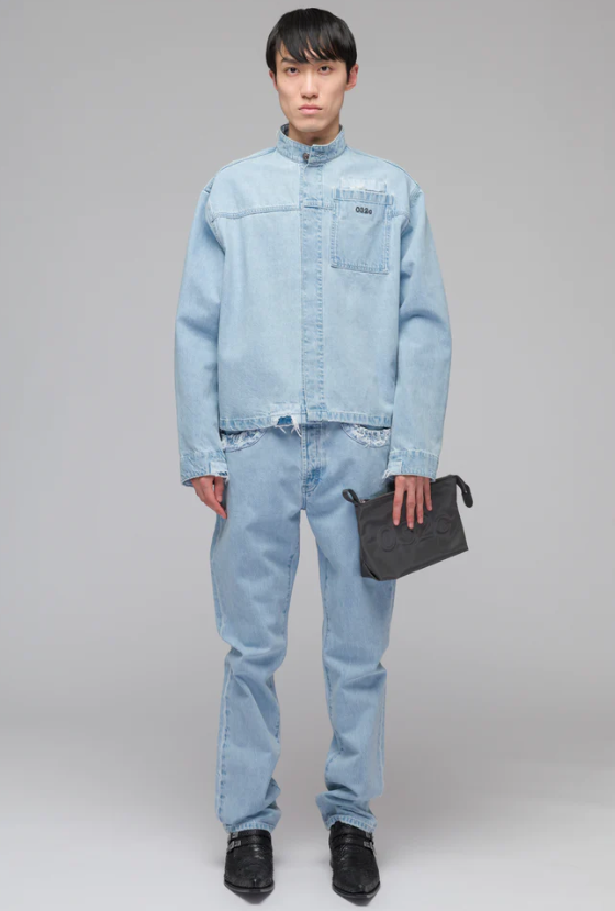 A man wearing a 032c light-wash denim jacket and pants with a blue purse